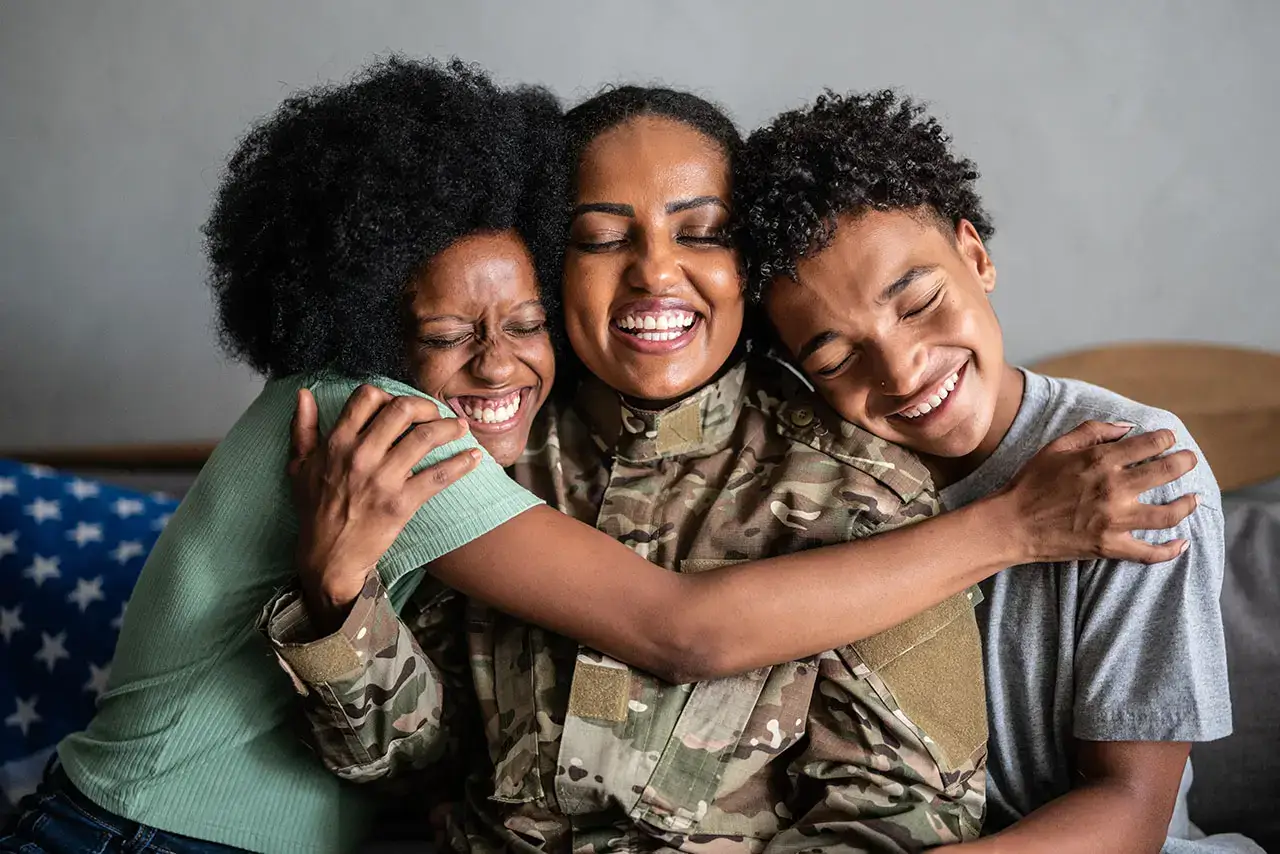 A student in their military uniform smiles as they receive hugs from their family.