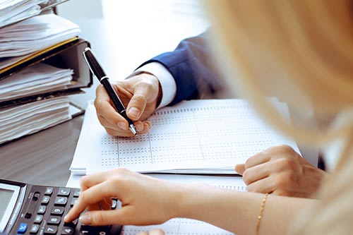 photo of a hand holding a pen and typing on a calculator