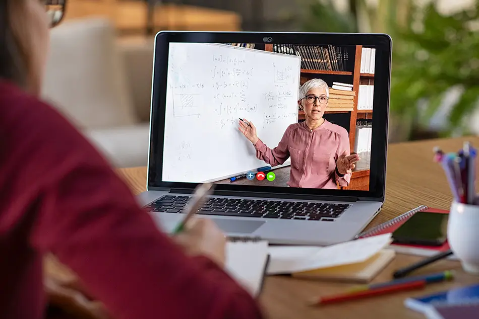 A student looks at their computer screen while a professor presents coursework via a video call.