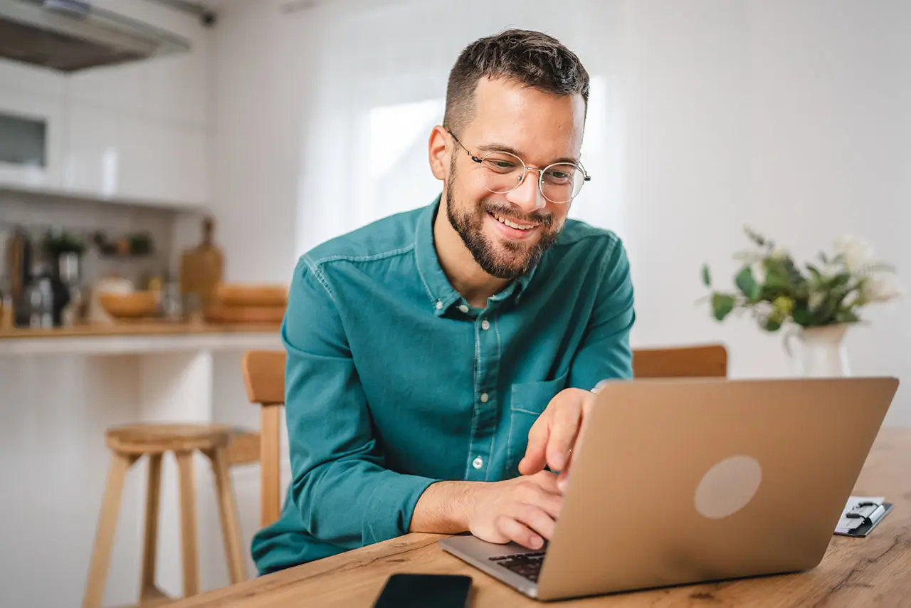 Male online student studying on laptop at kitchen table.